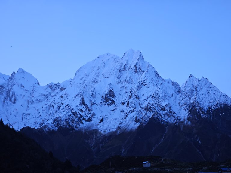 A majestic snow-capped mountain range under a clear blue sky, showcasing rugged peaks and steep slopes.