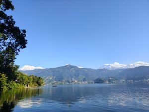 A serene landscape featuring a calm fewa lake reflecting the clear blue sky.