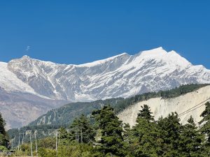 A majestic snow-capped mountain range under a clear blue sky, with rugged peaks and sharp ridges.
