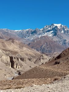 A panoramic view of a mountainous landscape featuring rugged terrain with shades of brown and gray.
