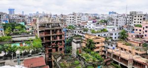 A dense urban landscape with a mix of completed and unfinished buildings, scattered greenery, and a cloudy sky, showcasing the blend of modern and older architecture in a growing city.