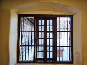 A traditional wooden window with vertical iron grills, opening to a tiled roof view inside Hill Palace Museum, Thrippunithura, Kerala. 