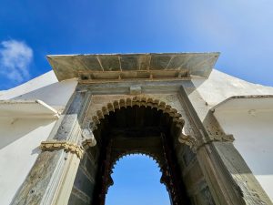 A close-up of the old arched stone doorway at Monsoon Palace, Sajjangarh, Udaipur. The photo is taken from below, showing the detailed carvings and blue sky above.