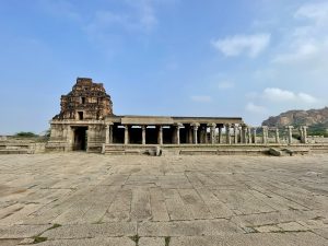 The main entrance and hall of Shree Vijay Vitthala Temple, Hampi, Karnataka, with stone pillars and a Gopuram in view. The temple architecture reflects the rich history of the Vijayanagara Empire. 