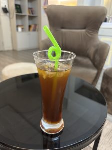 

A cold Americano with ice and a green straw on a table.