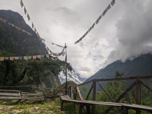 A serene mountain landscape features colorful prayer flags strung across a wooden structure. 