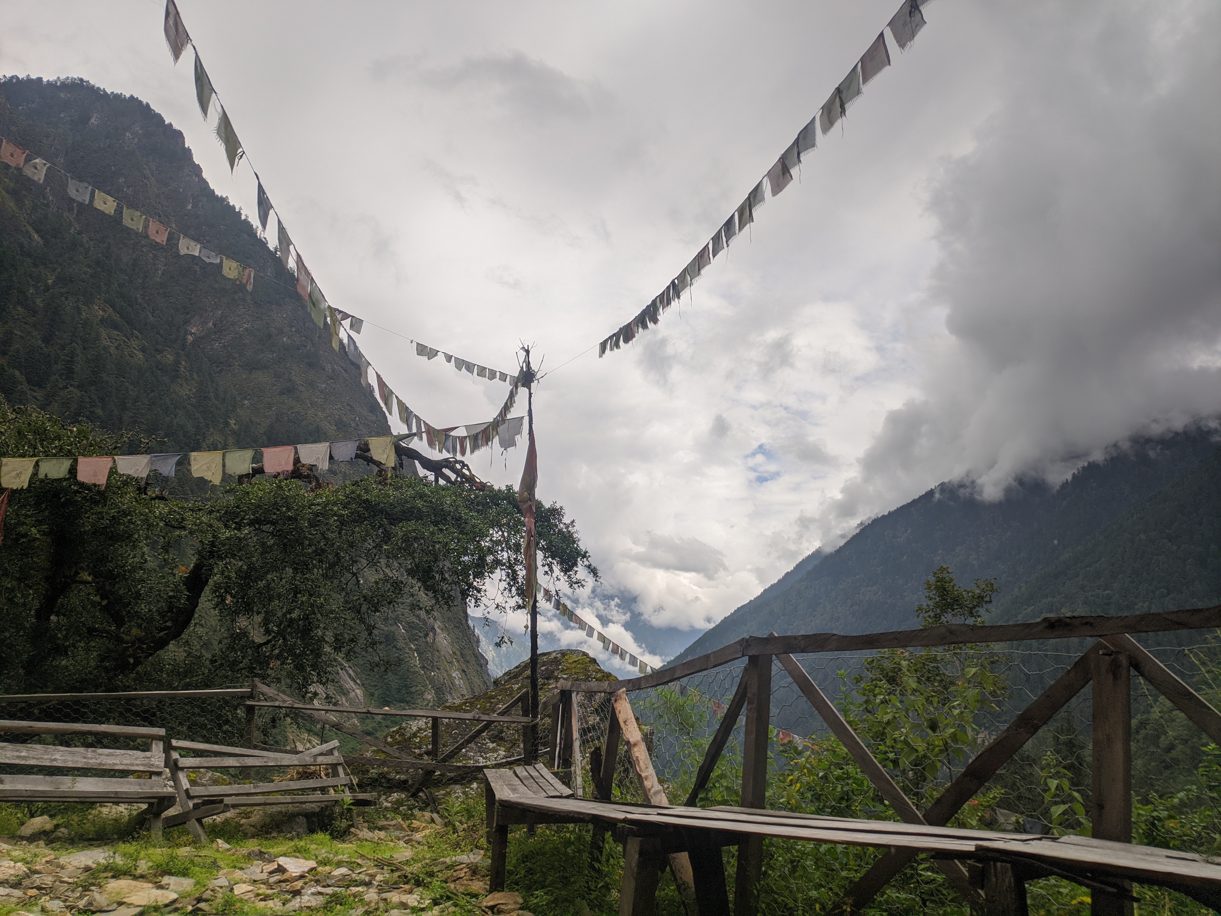 A serene mountain landscape features colorful prayer flags strung across a wooden structure.