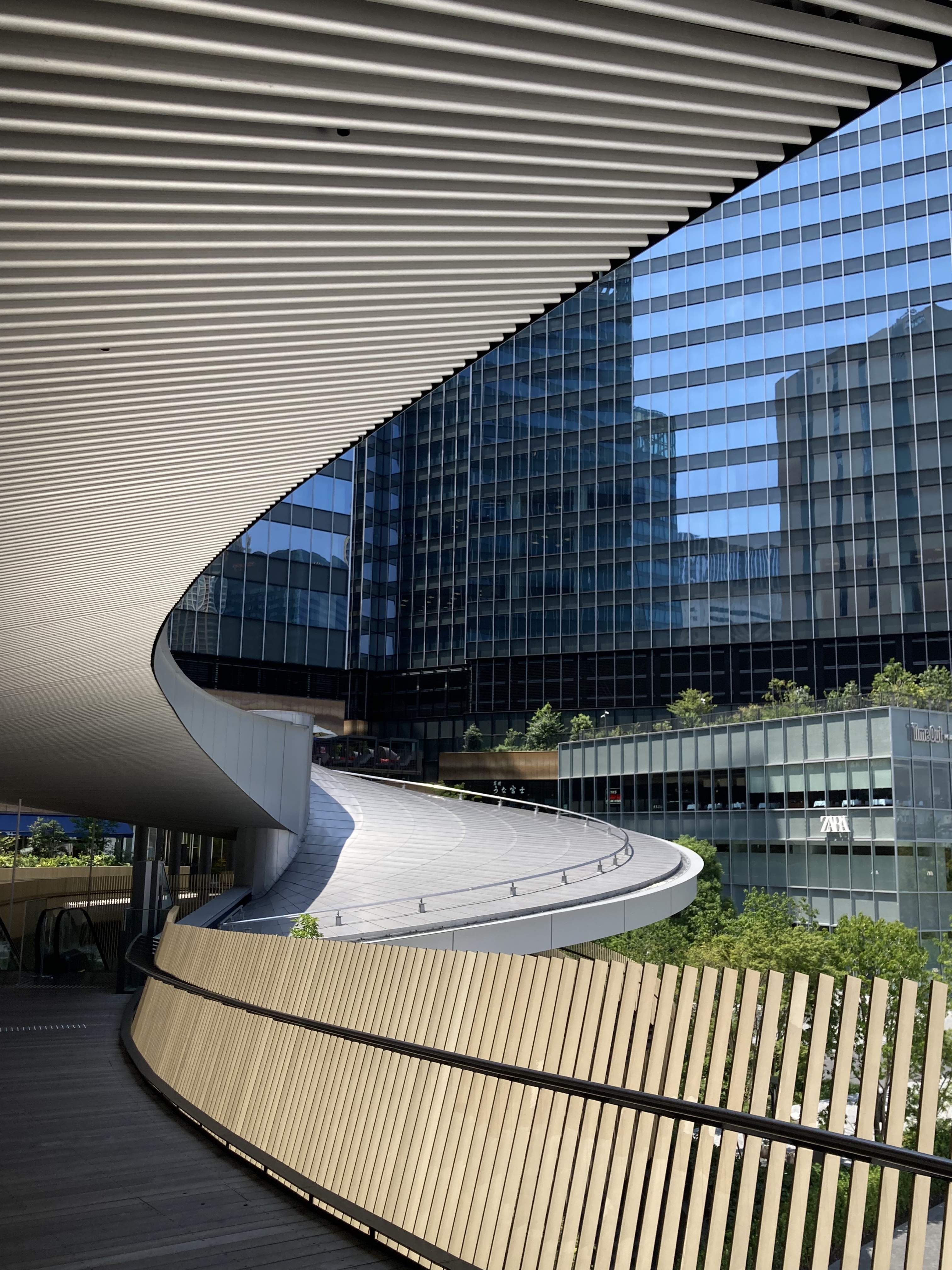 A modern architectural scene featuring a curved metallic walkway and a wooden railing.