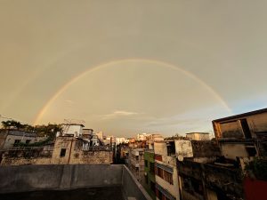 A breathtaking view of a double rainbow arching over the skyline of Dhaka Bangladesh in the early morning. The soft golden light of dawn enhances the beauty of the rainbows, creating a peaceful and magical atmosphere above the city rooftops