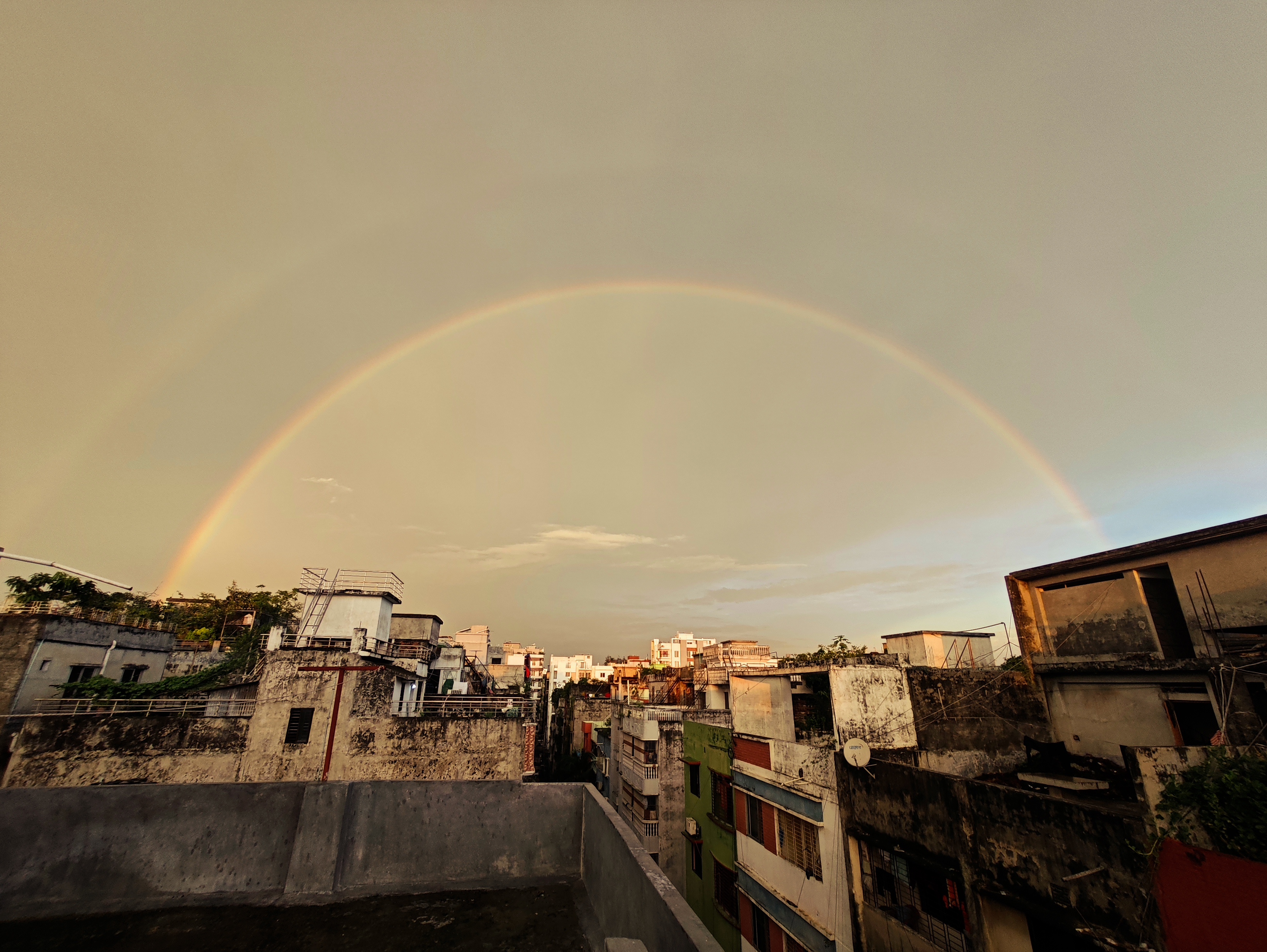 A breathtaking view of a double rainbow arching over the skyline of Dhaka Bangladesh in the early morning. The soft golden light of dawn enhances the beauty of the rainbows, creating a peaceful and magical atmosphere above the city rooftops