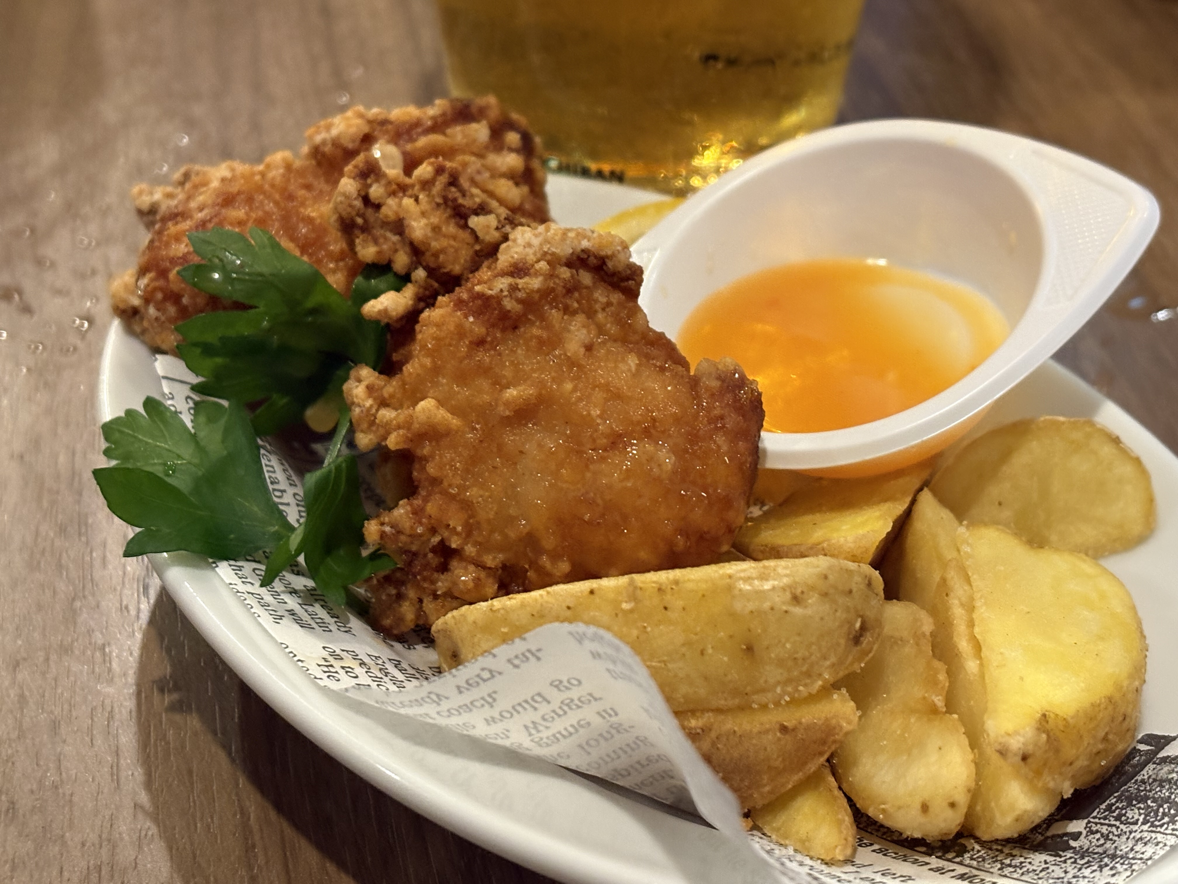 A plate of crispy fried chicken pieces, garnished with fresh parsley, accompanied by a small dish of dipping sauce and golden, roasted potato wedges.