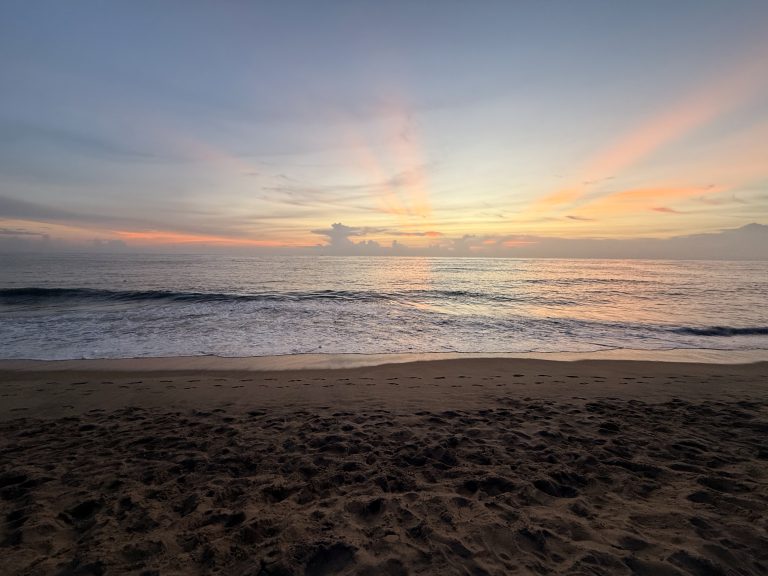 A scenic sunset at Cherai Beach, Ernakulam, with golden-pink rays reflecting on the sea and footprints in the sand.