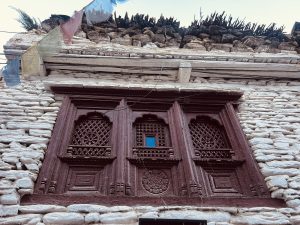 A close-up view of a traditional building made of white stones, featuring intricately carved wooden windows painted in a deep reddish-brown color. 

