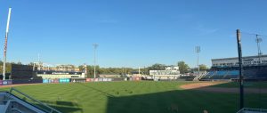 A baseball field in a minor league stadium. The sun is low, so half the field is in shade. Some equipment is set up in the outfield for guests to play lawn games. Grand Rapids, Michigan.