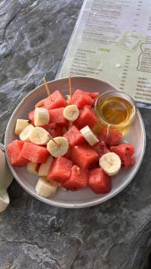 A plate of fresh fruit featuring cubes of watermelon and sliced banana, with toothpicks in some of the watermelon pieces.