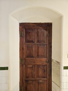 An old, carved wooden door with a classic design is seen inside the Hill Palace Museum, Thrippunithura, Kerala. The door adds a rustic charm to the heritage interior. 