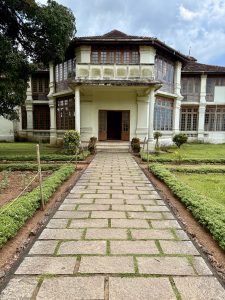 A wide stone pathway leads to the main entrance of Hill Palace, Thrippunithura. The symmetrical building and the garden on both sides create a royal and peaceful scene. 