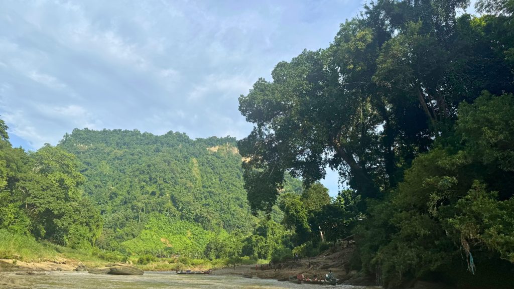 Beautiful Sangu River flowing through the lush green hills of Bandarban, surrounded by dense forest and a calm, cloudy sky.