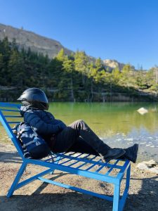 
A person wearing a black helmet is reclining on a blue lounge chair by a serene dhumba lake.