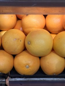 A neatly arranged bunch of grapefruit with golden-orange skin, stacked under a fluorescent light in a fruit shop in Palazhi, Kozhikode. 