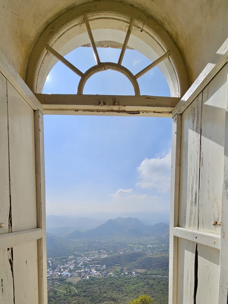 A scenic view of the Aravalli hills and a green valley seen through a half-arched open window at Monsoon Palace, Sajjangarh, Udaipur, Rajasthan.