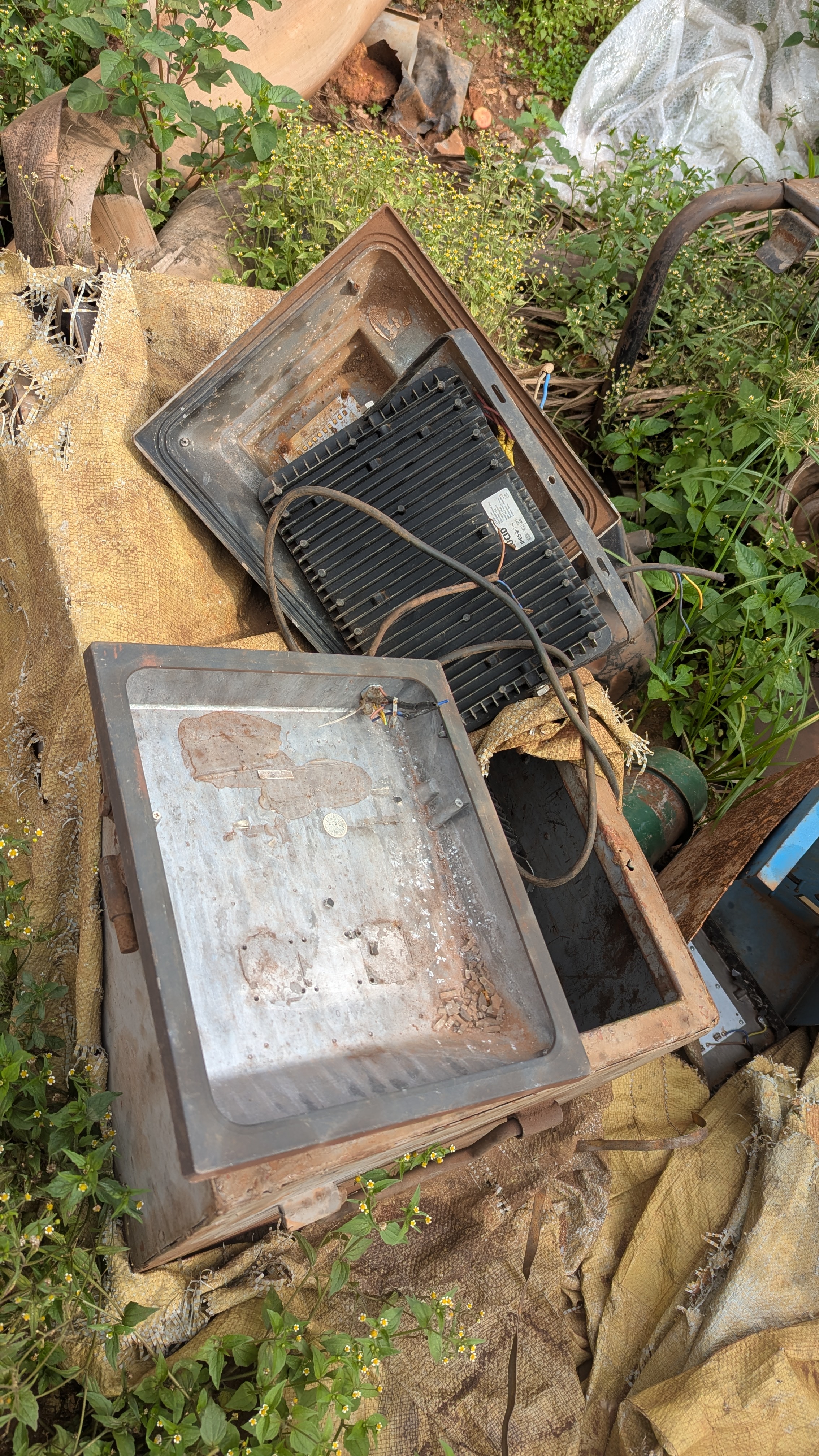 Electric lights at a disposal site.  The lights are rusted and broken, it looks like trash.