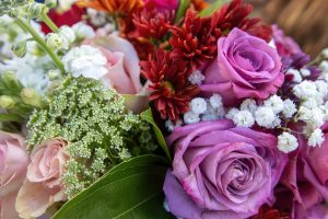 A close-up of a vibrant bouquet with pink and purple roses, red and orange blooms, white flowers, and lush green foliage.