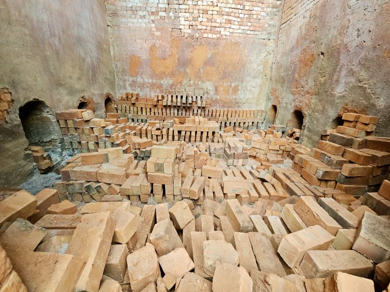 View inside a traditional kiln, where fired bricks are arranged around fire holes, in Perumanna, Kozhikode, Kerala. Displays rustic textures and earthy tones.