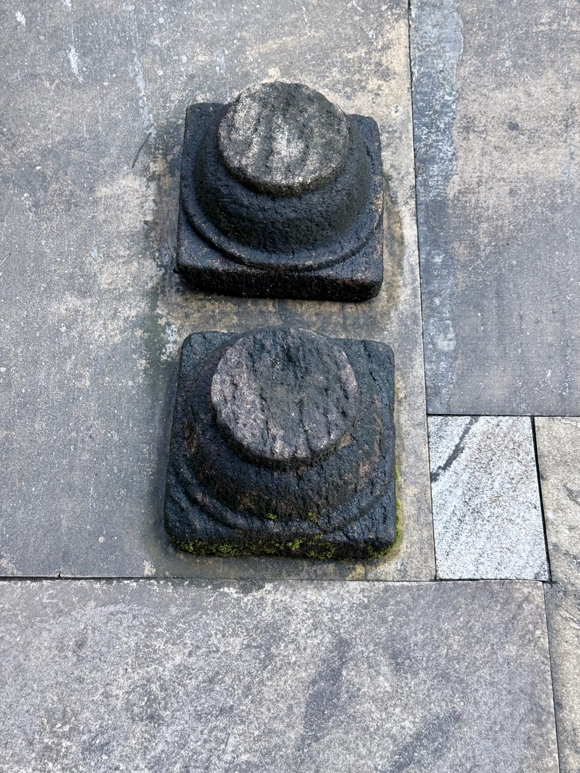 Two worn cylindrical stone pegs set in square bases, known as Balikallu, are used for making offerings to deities or spirits, photographed at Sree Shiva Vishnu Temple, Perumanna, Kozhikode.