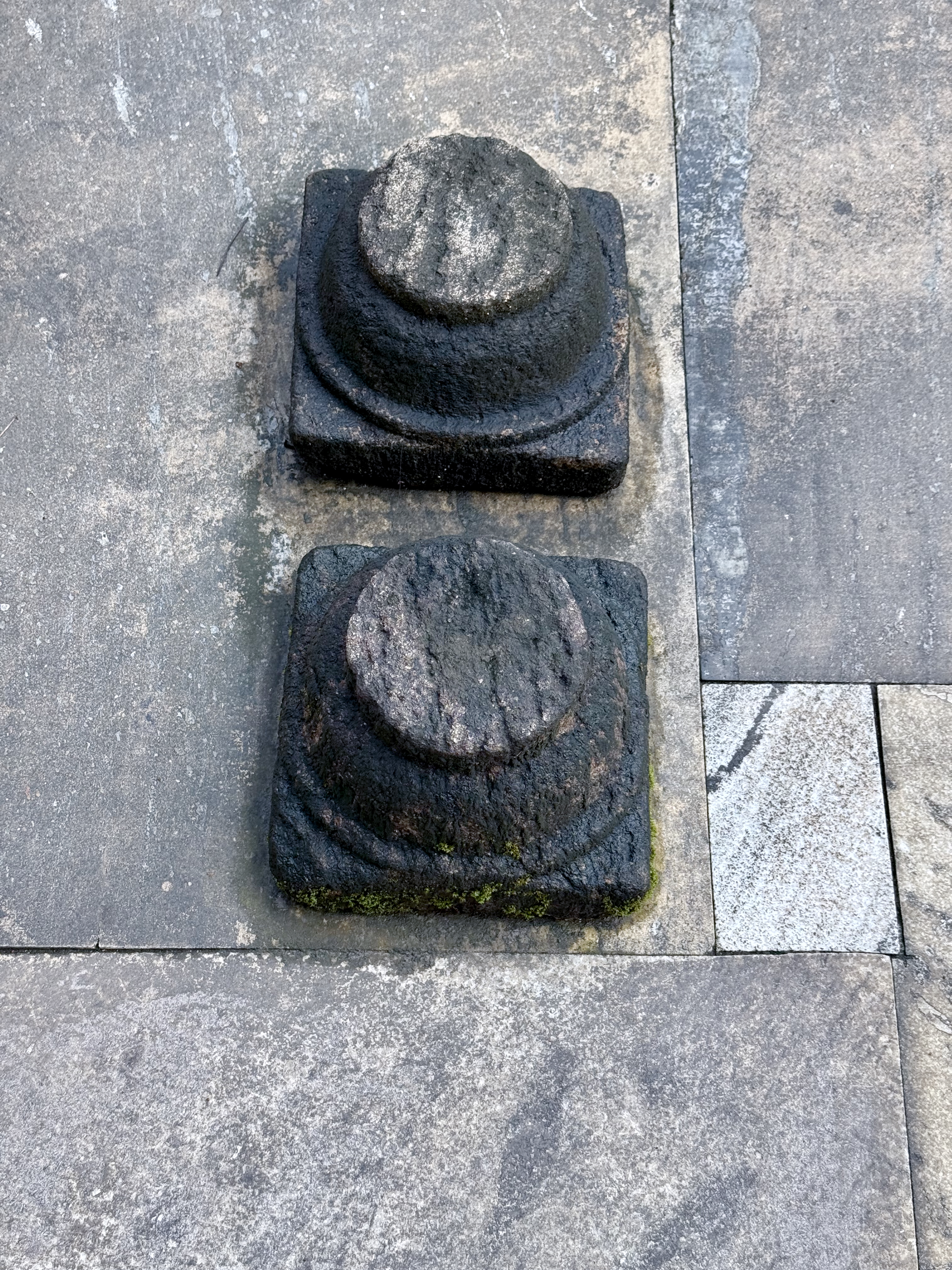 Two worn cylindrical stone pegs set in square bases, known as Balikallu, are used for making offerings to deities or spirits, photographed at Sree Shiva Vishnu Temple, Perumanna, Kozhikode.
