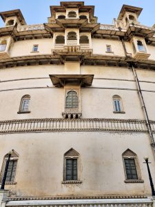 A side view of the City Palace in Udaipur in the evening, showcasing its beautiful architecture. The building features ornate balconies, arched windows, and decorative stone carvings.