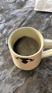 A close-up view of a beige mug with a frog silhouette on the side, filled with dark coffee.