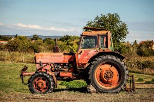 An old, rusty red tractor stands in a green field. 