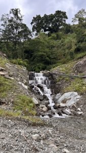 A small waterfall cascading down rocky terrain, surrounded by lush greenery. 