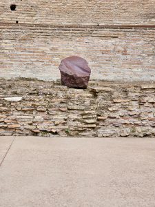 A single broken red stone piece sits neatly on an old Roman brick wall, offering a quiet moment among the ruins of the Roman Forum in Rome, Italy. 