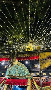 A beautifully decorated temple facade is illuminated with strings of warm white lights radiating outward, creating a starburst effect. 