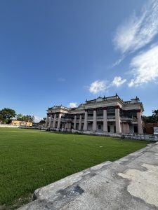 An image of a building with grassy field at front and blue sky in its background.