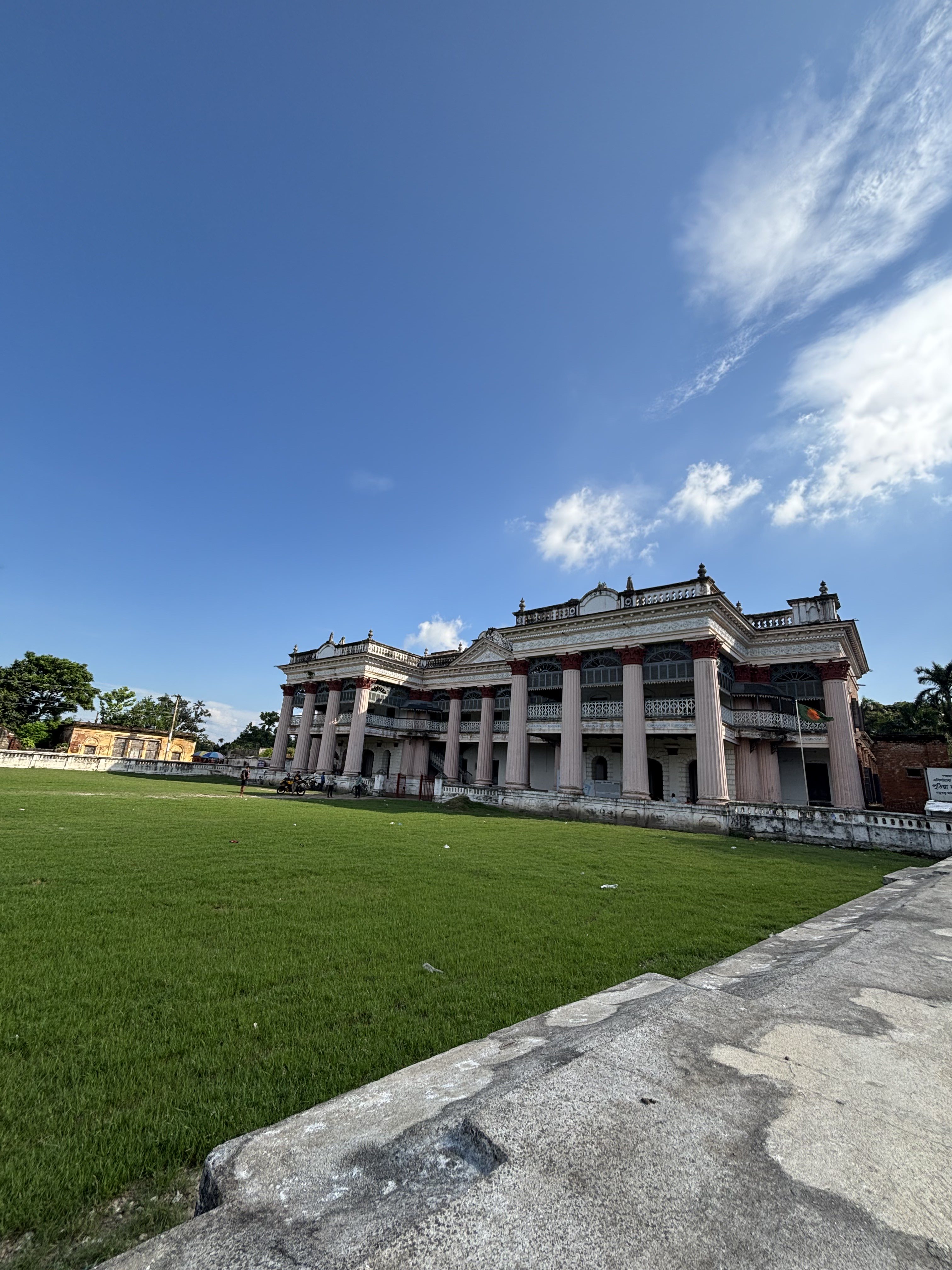 An image of a building with grassy field at front and blue sky in its background.