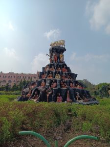 A wide view of a large sculptural mountain featuring numerous human figures in meditation poses, with a group of white cows positioned on the top.