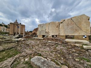Large broken stone slabs with Latin inscriptions lie among scattered ruins and ancient pillars inside the Roman Forum, preserving the memory of Rome’s imperial past. Captured from the Roman Forum, Rome, Italy.