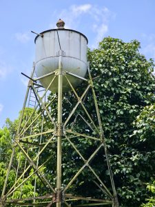 An elevated iron water tank with a rusted frame, standing above thick greenery. Photo taken at Hill Palace, Thrippunithura, Kerala.