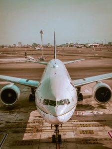 Front view of a commercial airplane parked on the airport runway with city buildings visible in the background.