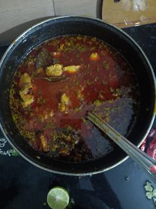 A black pot with tasty stew containing meat chunks and herbs in a thick red soup