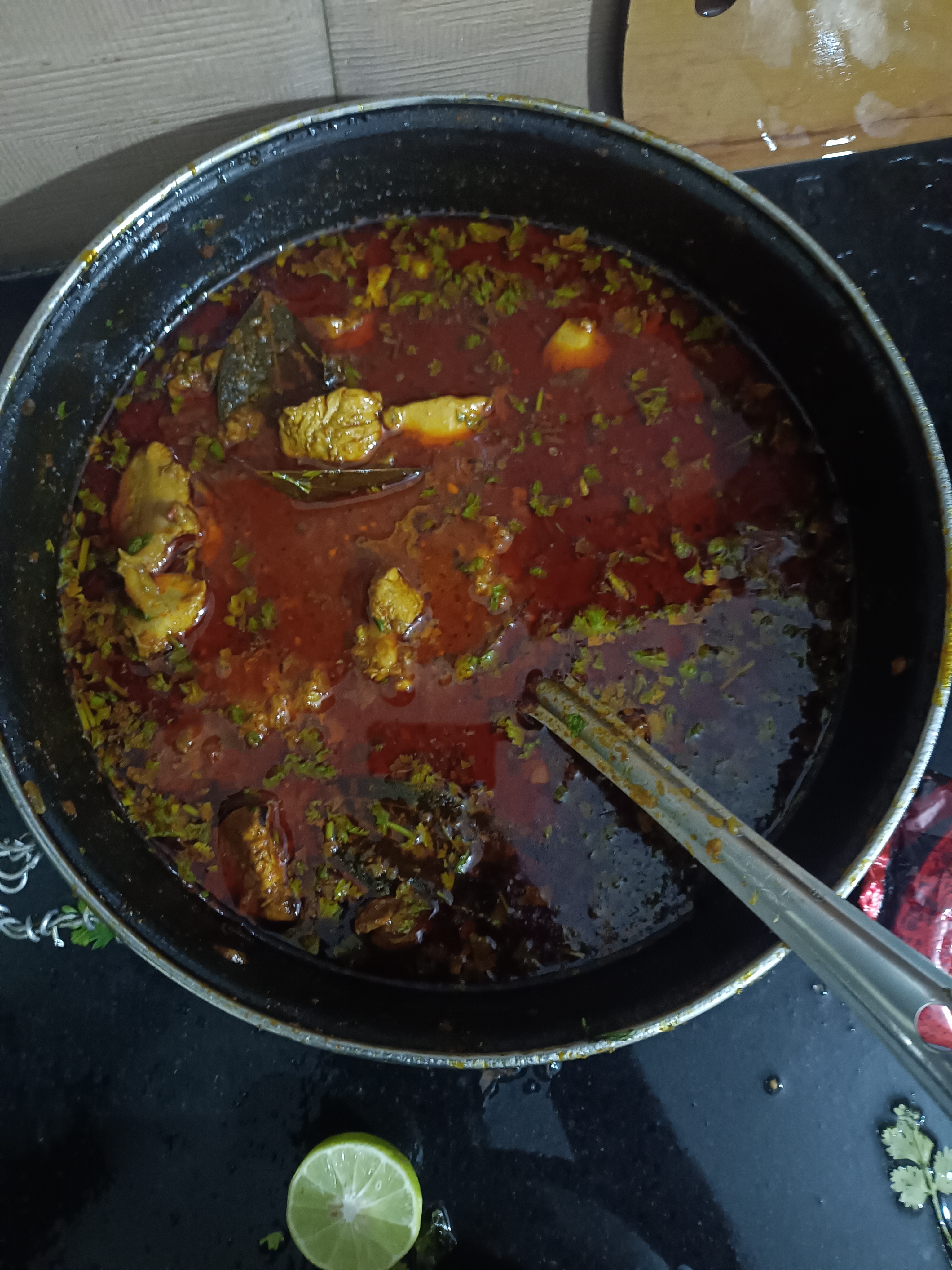 A black pot with tasty stew containing meat chunks and herbs in a thick red soup