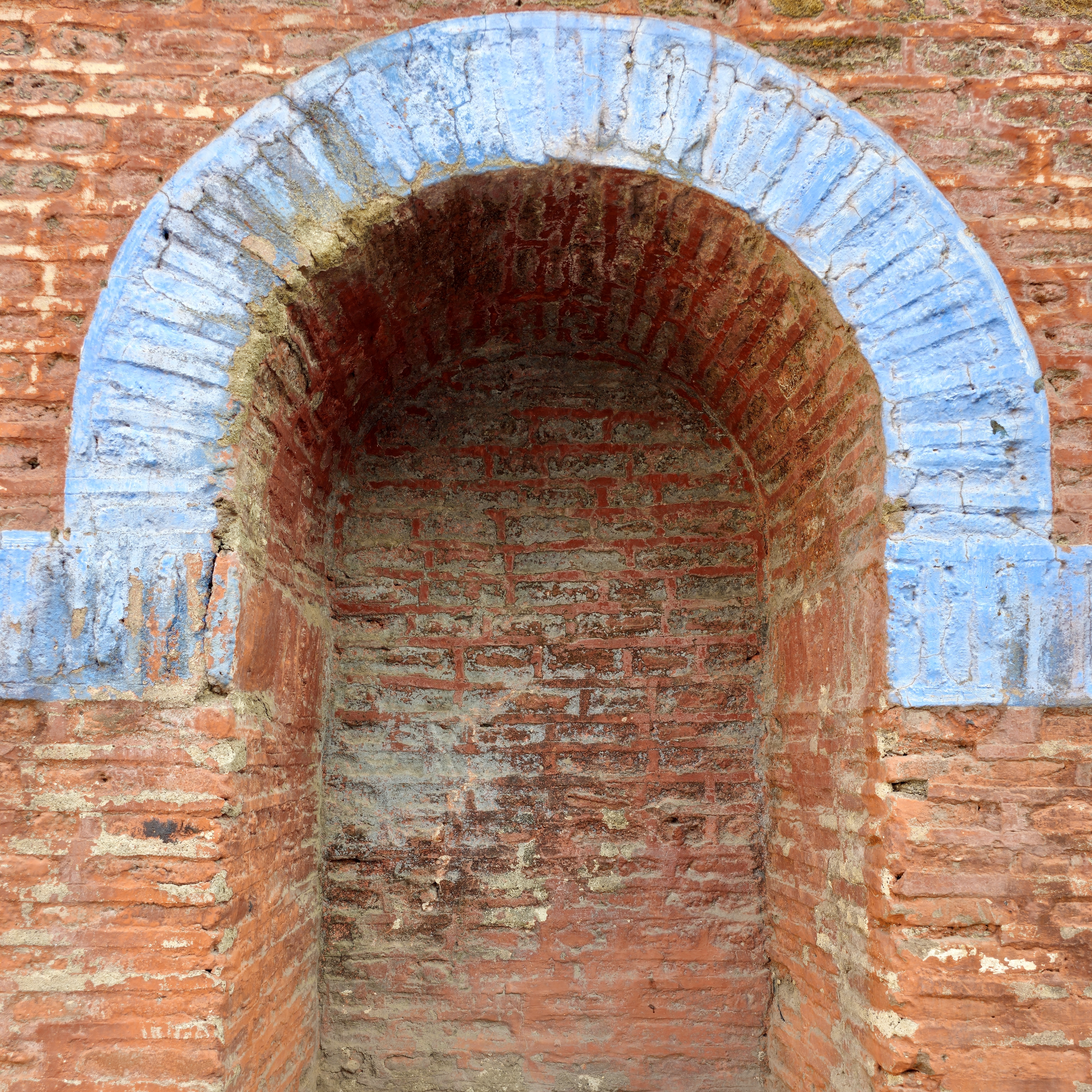 A worn-out arched brick niche with blue border detail at Parvati Hill, Pune. Shows rustic architectural texture and color. 