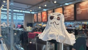 A closeup of a ghost made from a coffee filter.  In the background is a coffee shop, blurred.