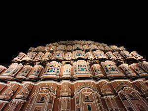 Upward night view of Hawa Mahal showcasing a five-story pink sandstone facade with 953 ornate windows and colorful stained glass in Jaipur
