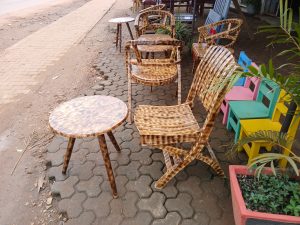 A collection of ornate, wooden chairs and tables is lined up along a sidewalk. 