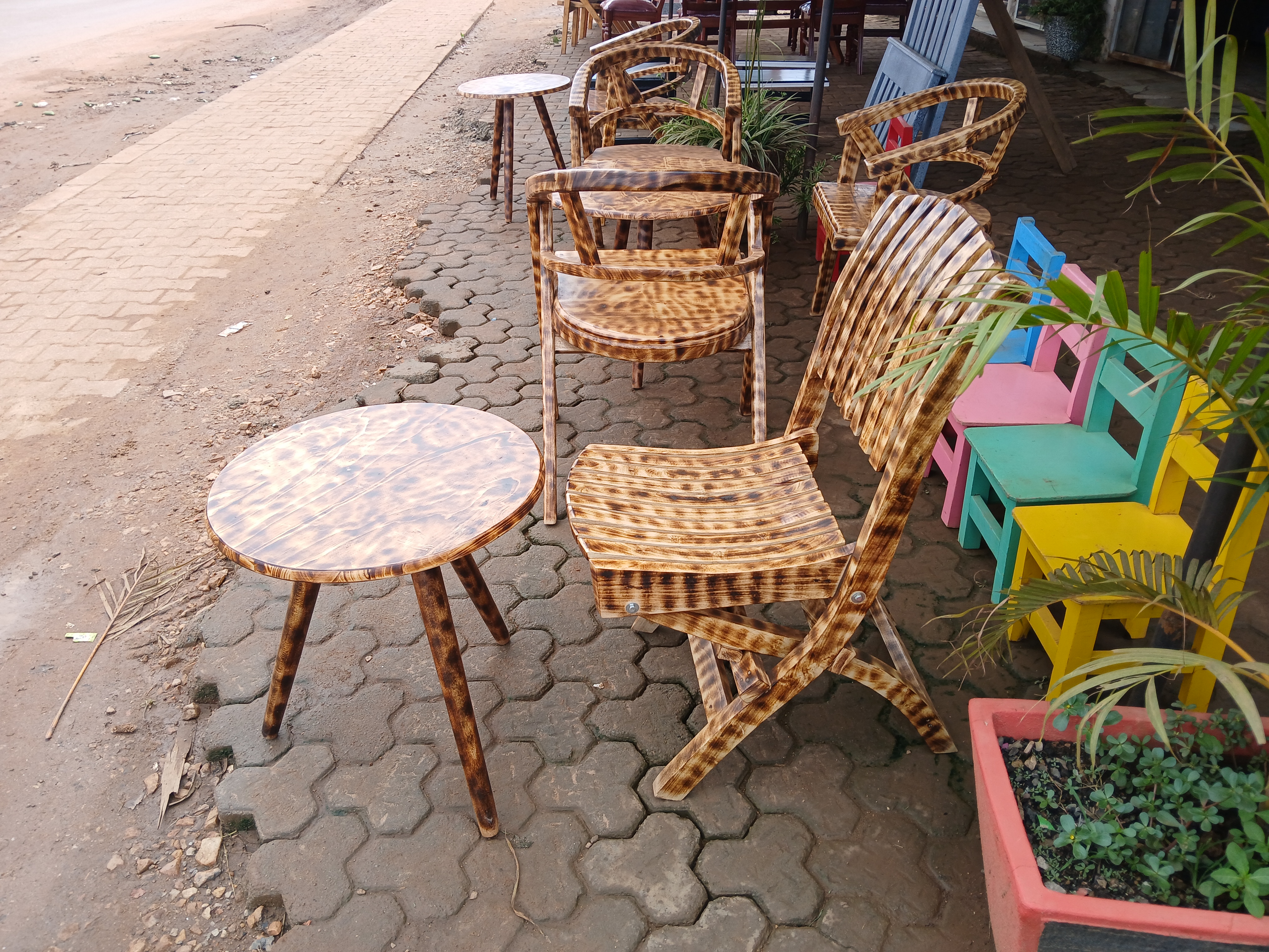 A collection of ornate, wooden chairs and tables is lined up along a sidewalk. 