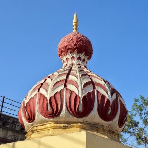 A dome-shaped temple element featuring red and white sculptural patterns with a golden finial on top. Clear blue sky in the background. Shot at Parvati Hill, Pune.